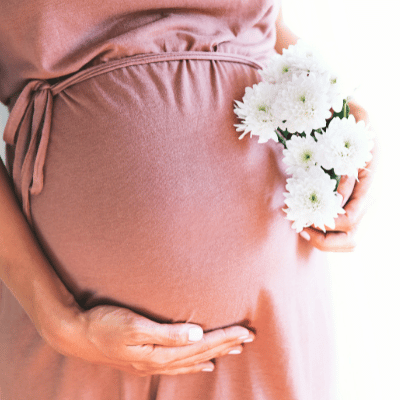 Cropped view of woman in pink dress holding flowers and pregnant belly